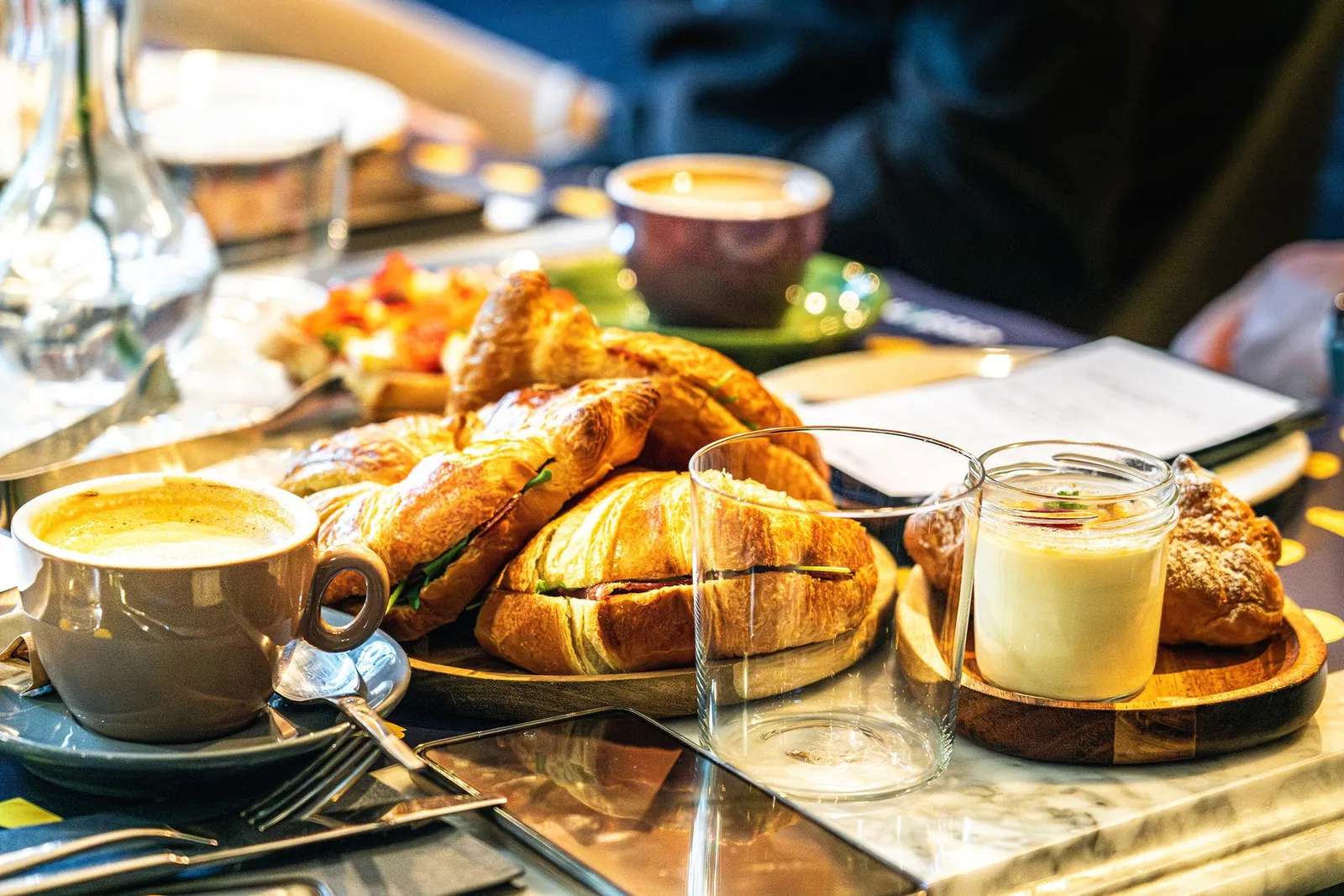 Café recién servido junto a croissants y pan dulce en una mesa de coffee break