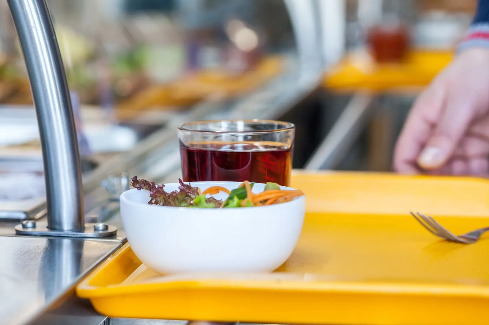 Charola amarilla con ensalada y bebida en la línea de servicio de un comedor