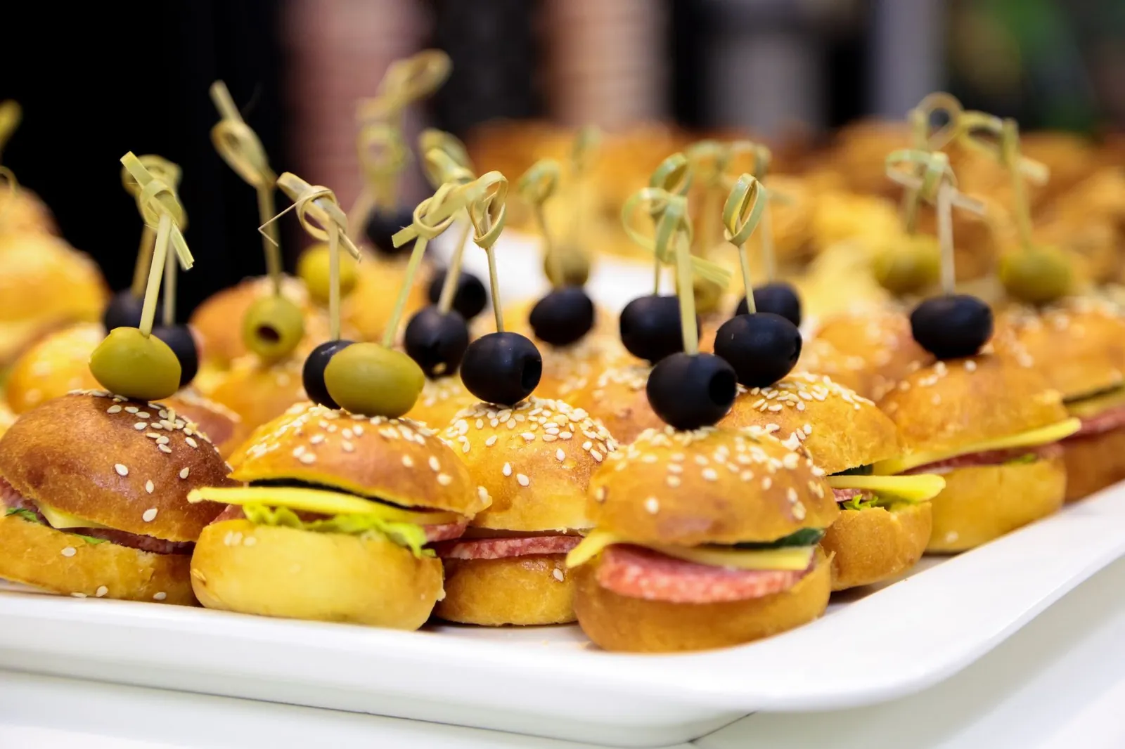 Bocadillos salados con aceituna en palillo sobre una charola blanca
