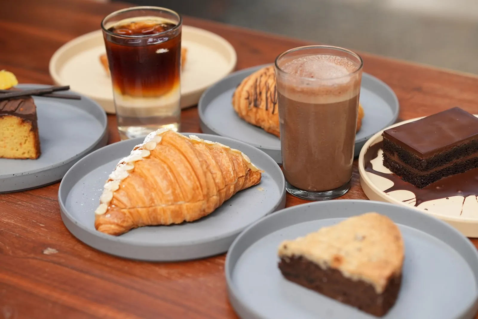 Café frío, chocolate caliente, croissant y rebanadas de pastel en platos individuales